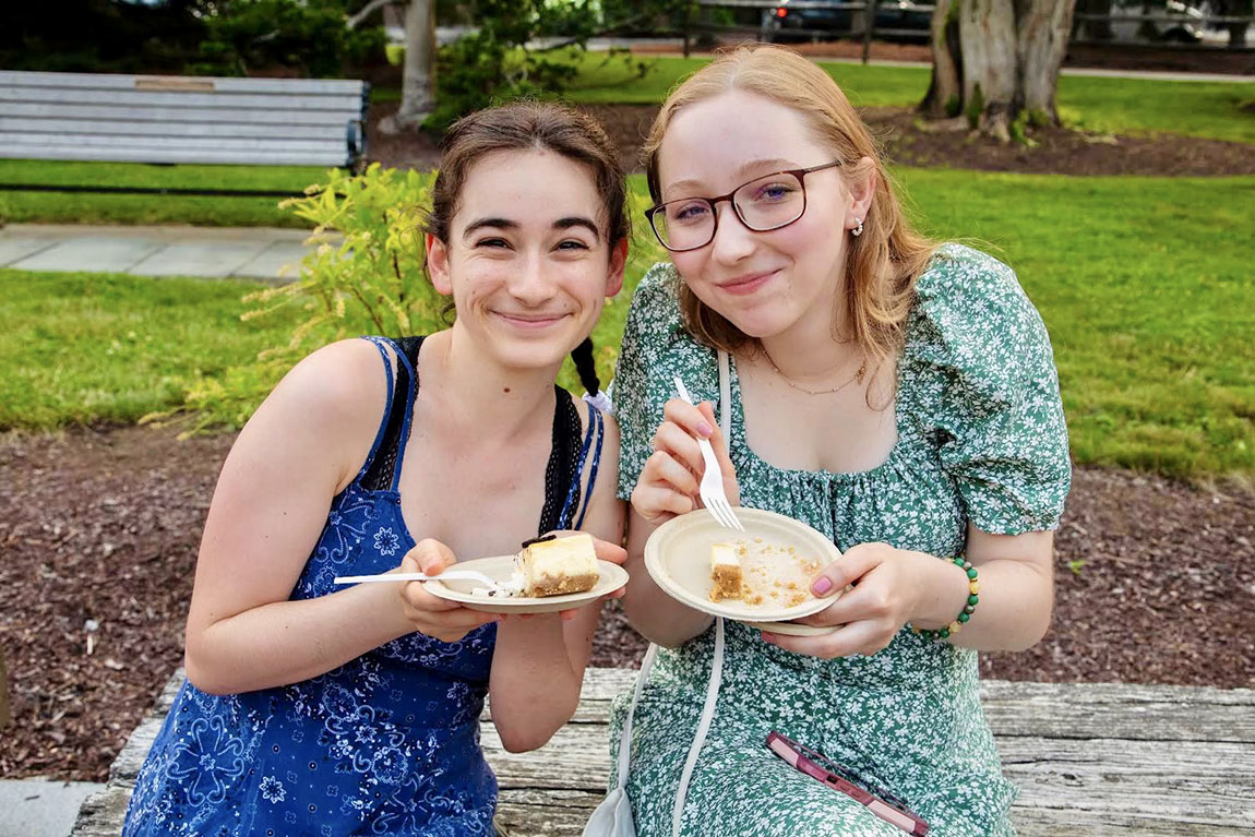 Two smiling young people hold plates of cake and look at the camera