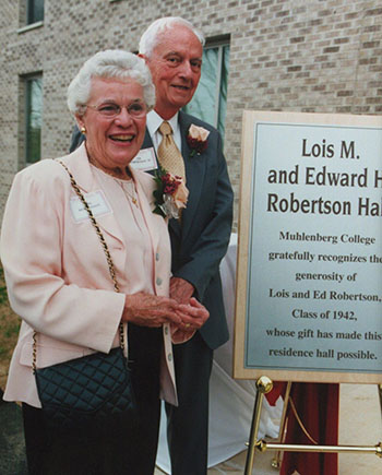 A man and a woman with white hair smile in front of a brick building in an archival photograph