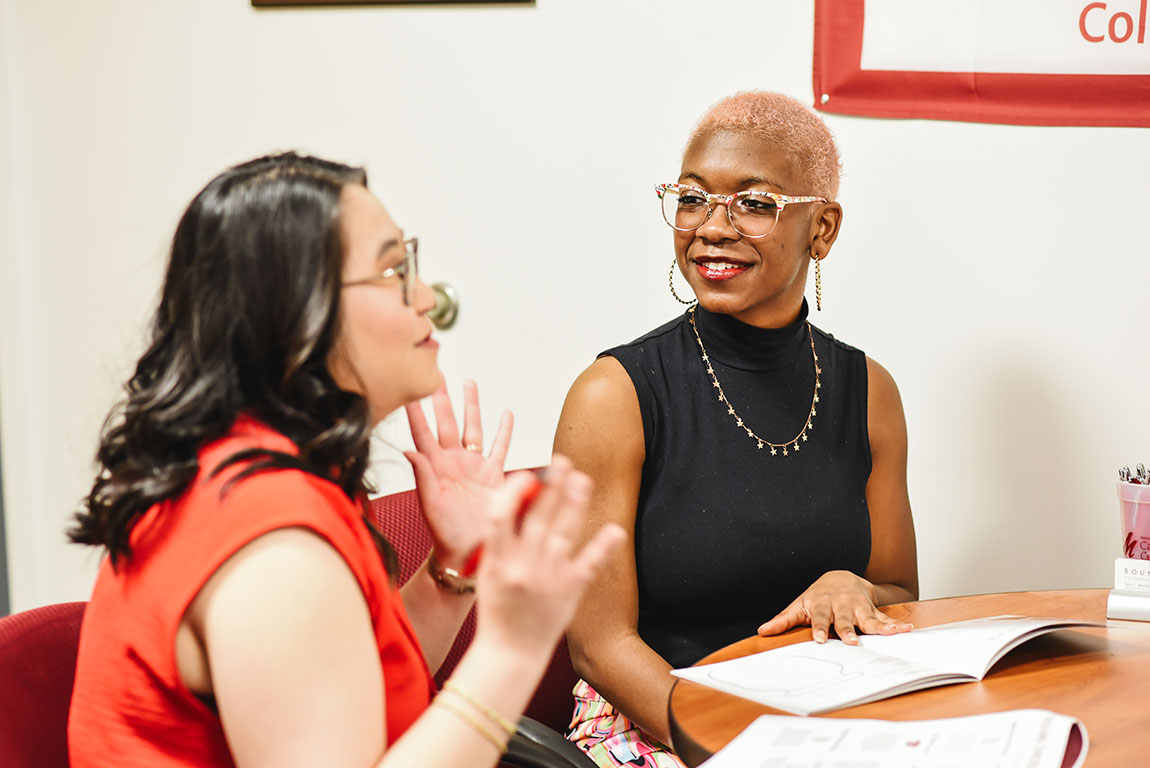 A college staff member speaks with a college student in a black shirt and glasses