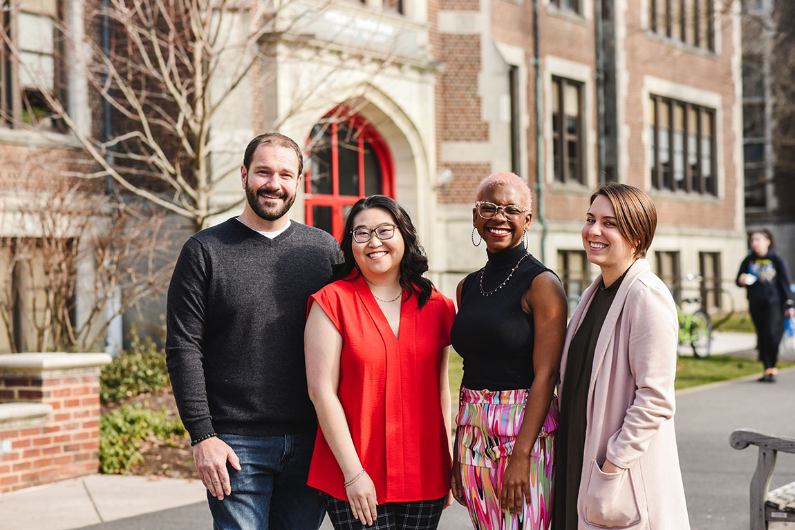 Three college faculty/staff and one student smile at the camera while posing outside