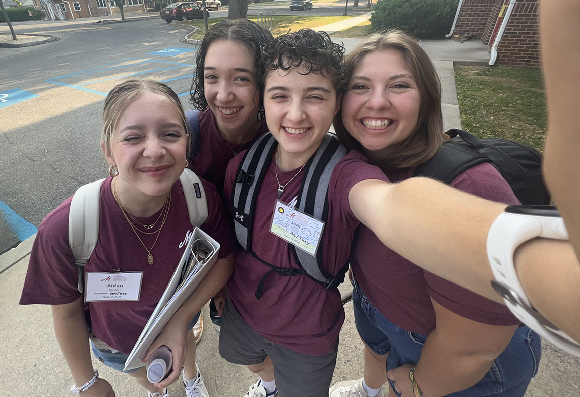 A group of three smiling college students in matching maroon T-shirts gather together and pose for a selfie
