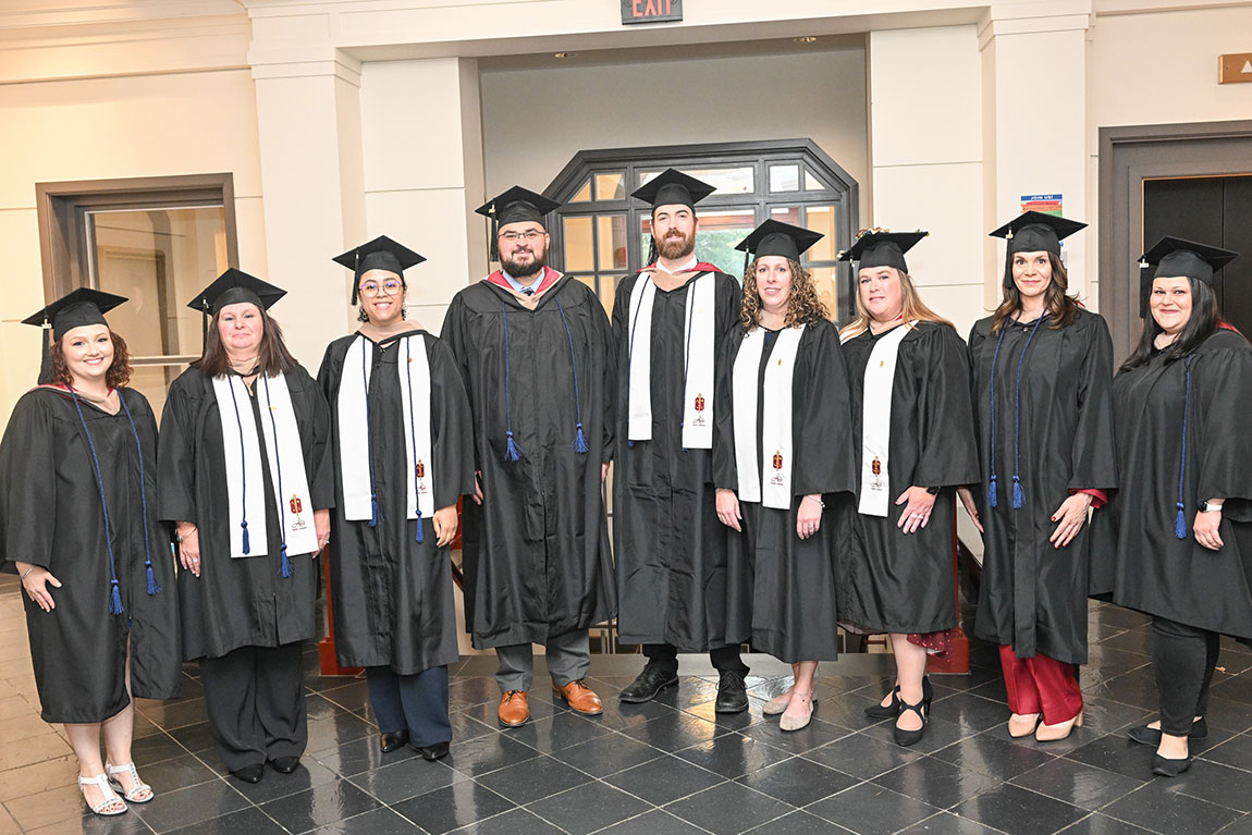 A group of adult learners and master's degree recipients in graduation garb smiles for the camera