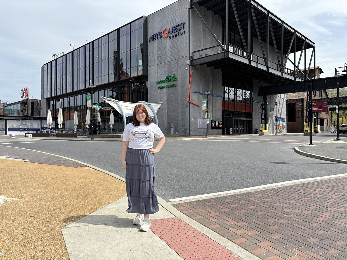 A college student stands outside a building that says ArtsQuest
