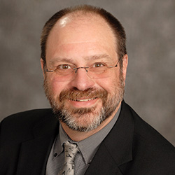 A headshot of Eduardo Azzati, who has glasses and facial hair and is wearing a suit