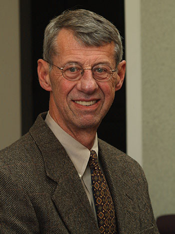 A male professor in a jacket and glasses smiles for a headshot