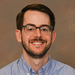 A headshot of Hunter Holt, who has short brown hair and facial hair and glasses