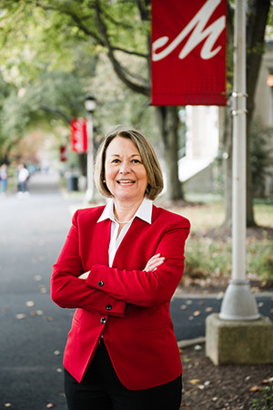 A headshot of a smiling woman in a red blazer standing with her arms crossed on Academic Row