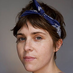 A headshot of Kiah Bennett, who has short dark hair and is wearing a blue bandana tied around it