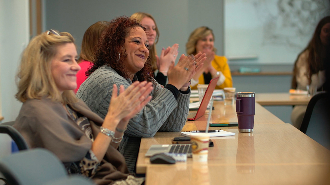 Students in the diversity, equity, inclusion and belonging graduate certificate program sit at a table and applaud