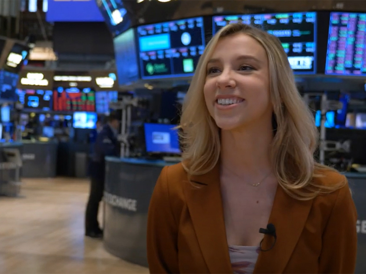 A  woman dressed professionally smiles on the floor of the New York Stock Exchange.