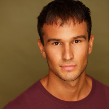 A man in a dark maroon shirt looks at the camera.