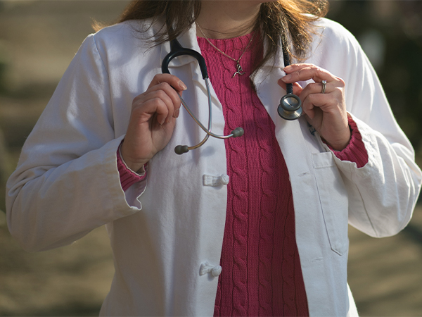 A close-up of a person wearing a lab coat with a stethoscope draped around the neck.
