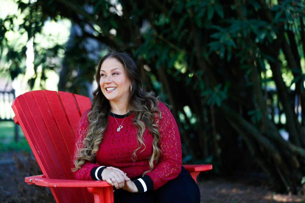 A smiling Muhlenberg graduate student sits on a red Adirondack chair
