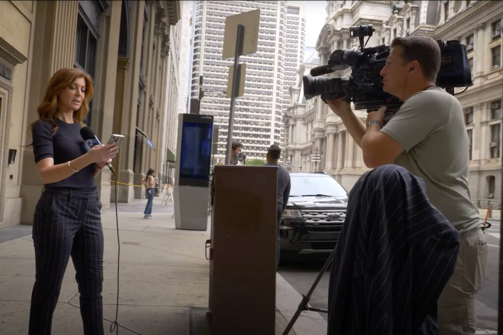 A broadcast journalist and a cameraman prepare to shoot on a city street