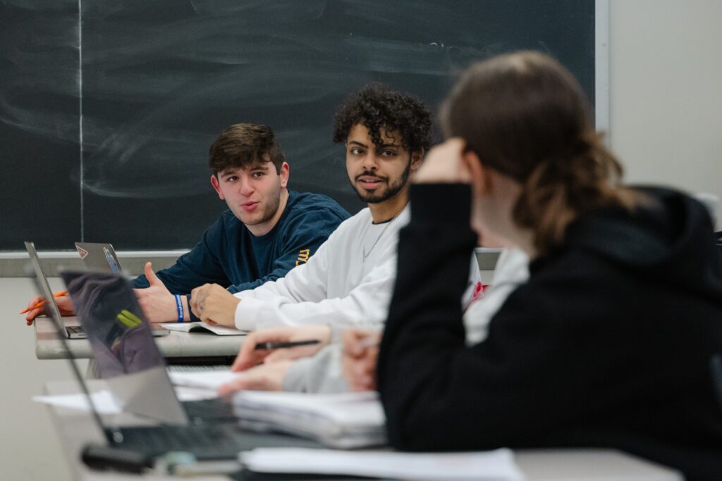 Three students sitting in a classroom talk to each other.