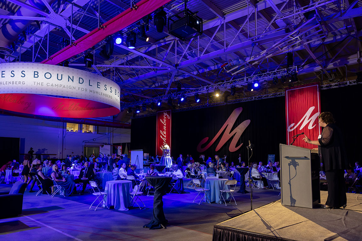 A view from behind the podium at a gala with a large red M hanging on the wall