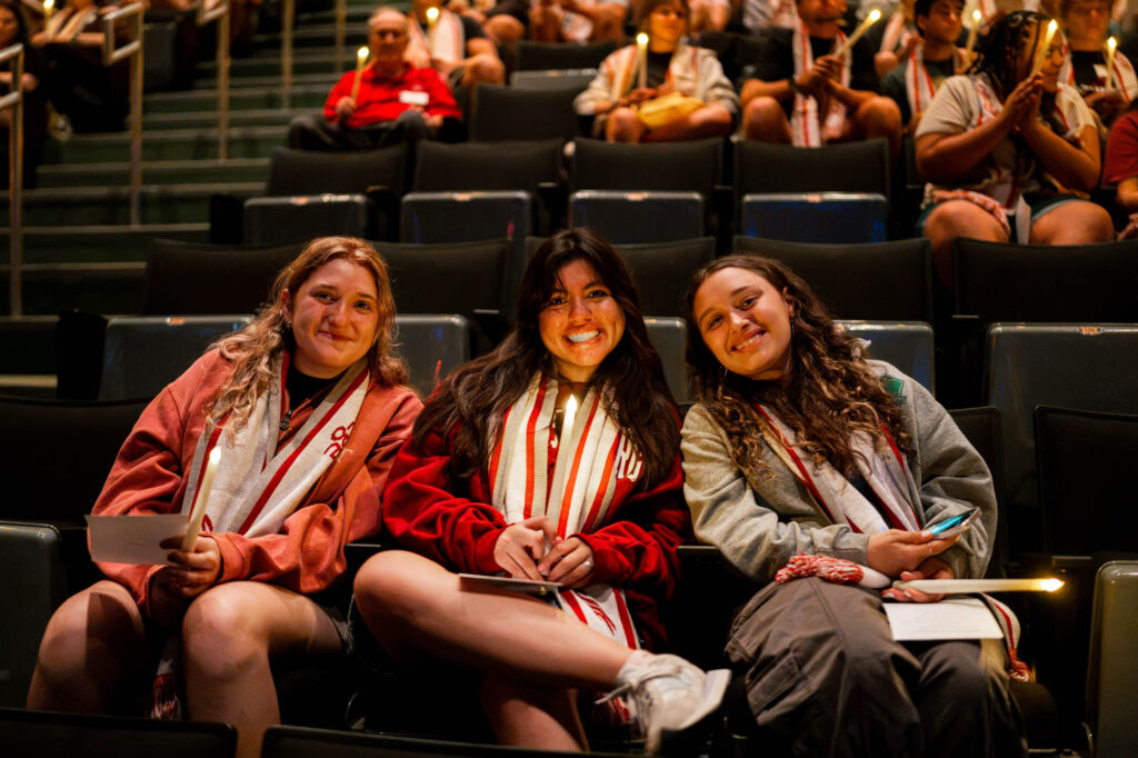 Three new Muhlenberg College students smile in auditorium seats