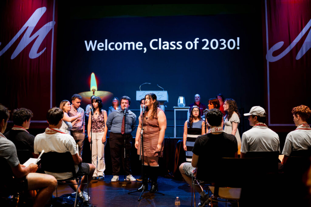 Muhlenberg College students sing in front of a screen that says Welcome, Class of 2030!