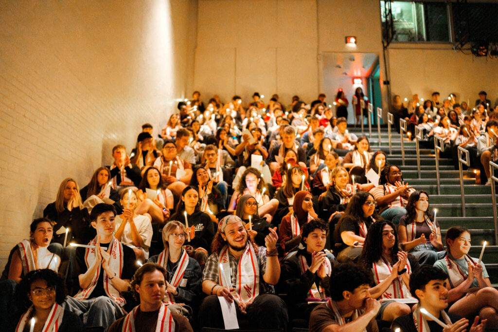 New Muhlenberg College students hold battery-operated candles while seated in an auditorum
