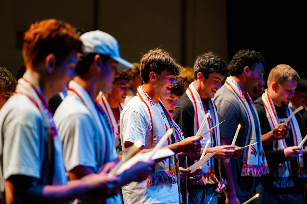 New Muhlenberg College students standing in a row sing while holding battery-operated candles