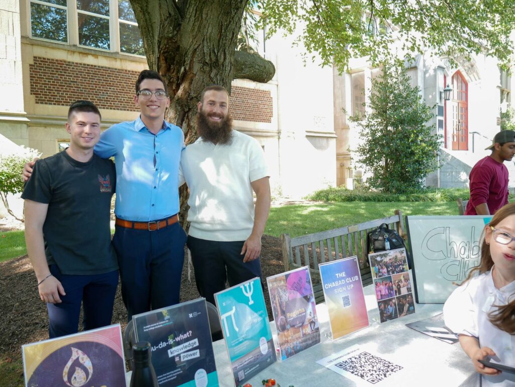 Three college students stand behind a table that says Chabad Club