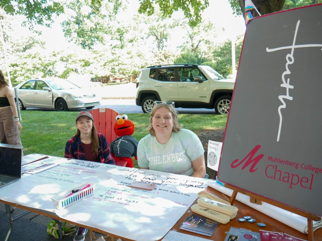 Two college students sit at a table with a sign that says Muhlenberg College Chapel