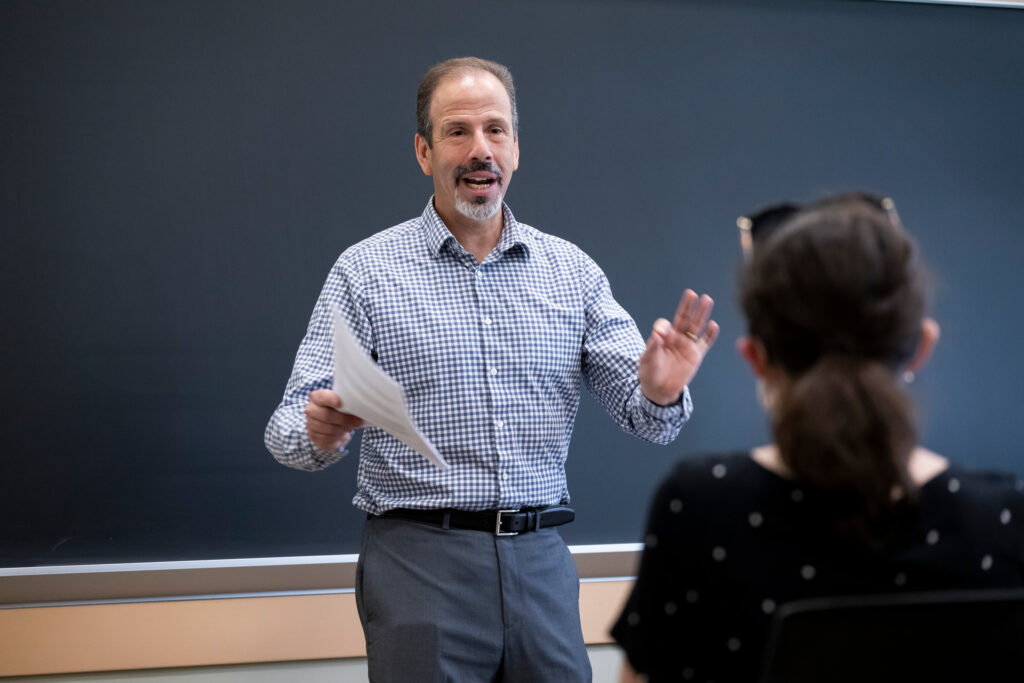 A college professor in a checked button-down shirt teaches a class