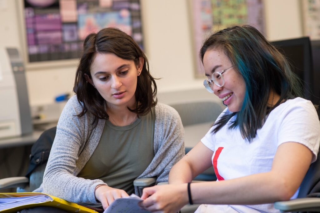 Two students in a classroom look at a book.