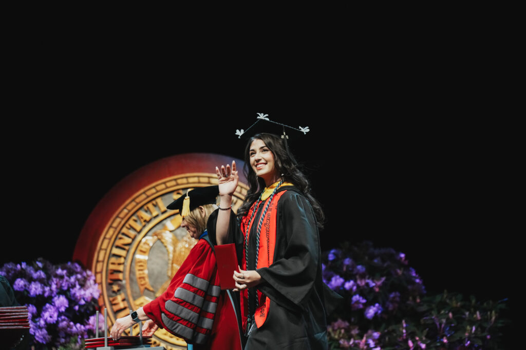 A college gradaute walks the stage at commencement and waves