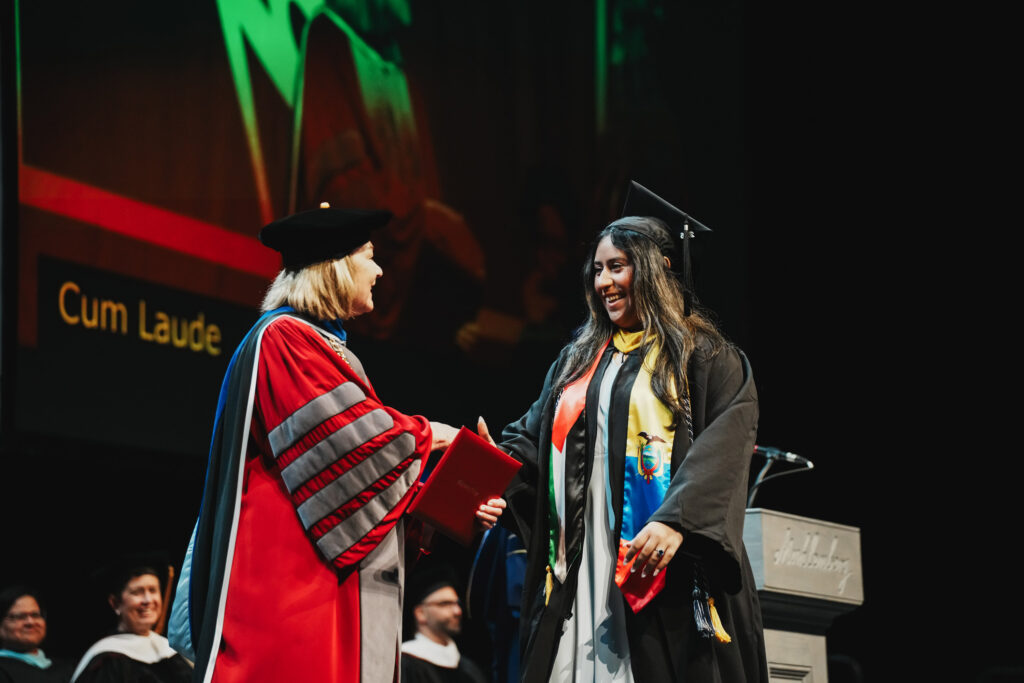 A college gradaute walks the stage at commencement and shakes hands with the college president