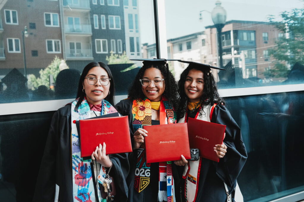 Three college graduates pose with their diplomas after commencement