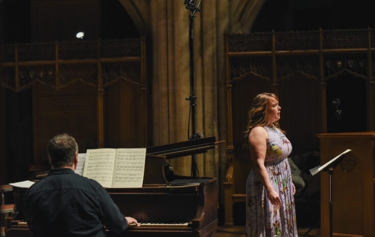A singer performs in a chapel next to a pianist playing a grand piano