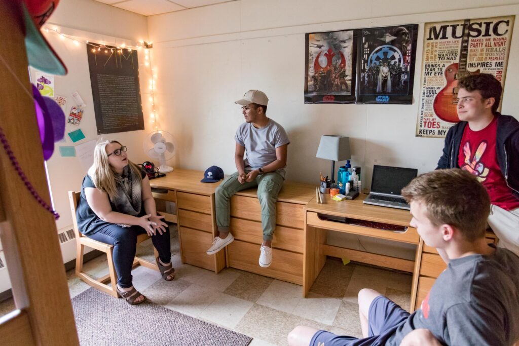 Four college students sit in a dorm room and talk about campus life