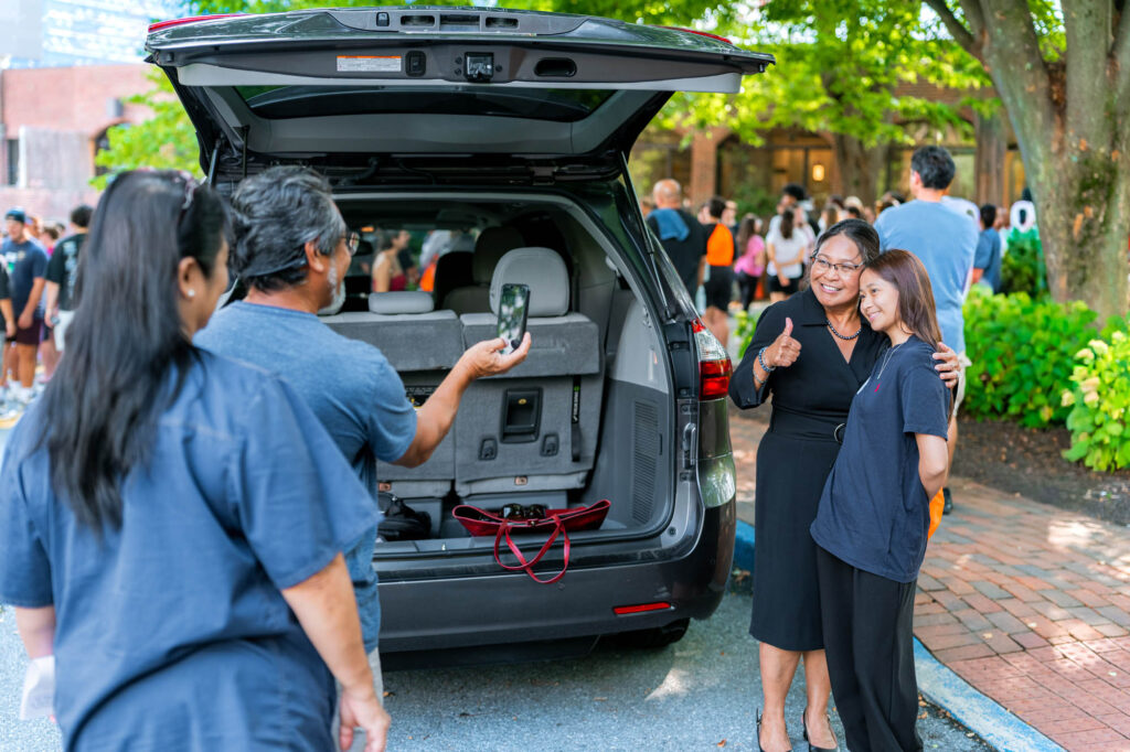 A Muhlenberg student poses with family in front of an open car trunk during orientation