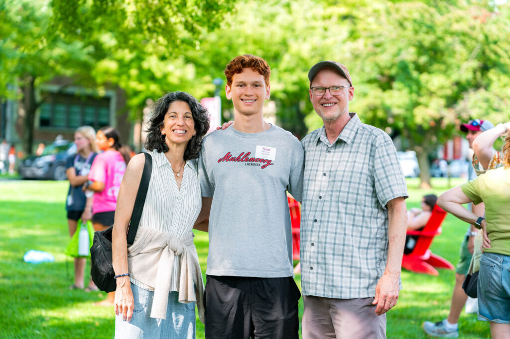 Two Muhlenberg College parents get a photo with their student wearng a Muhlenberg lacrosse shirt during orientation