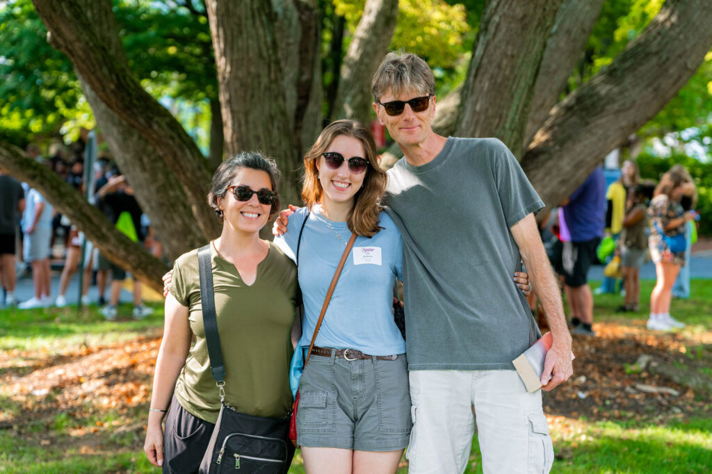 Two Muhlenberg College parents get a photo with their student, all of them in sunglasses, during orientation