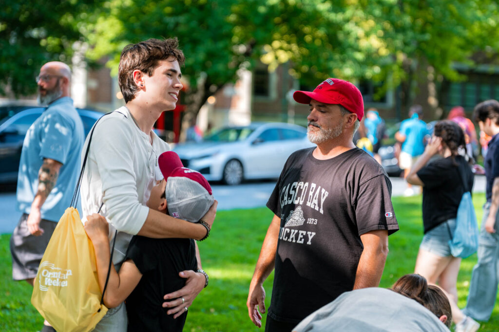 Two siblings hug while their father looks on during Muhlenberg College orientation