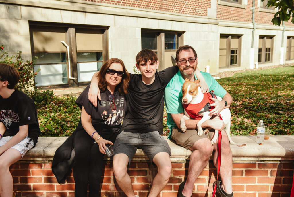 A student and his parents with a dog on a college campus during Family Weekend