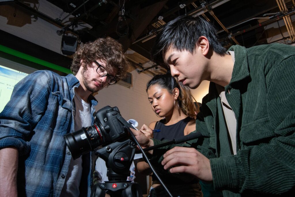College students gather around a camera in a studio.