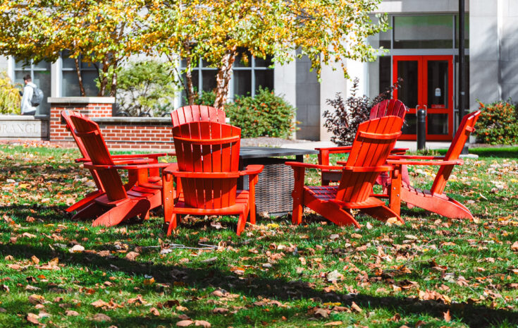 A circle of red Adirondack chairs around a fire pit