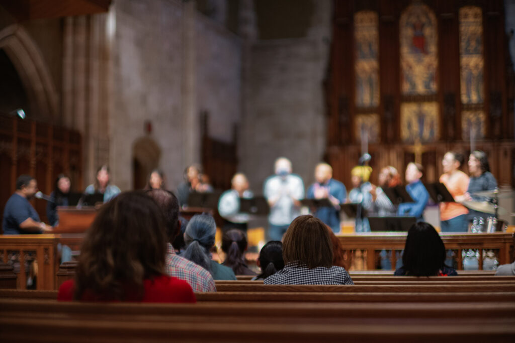 People sit in a chapel while people sing on the altar
