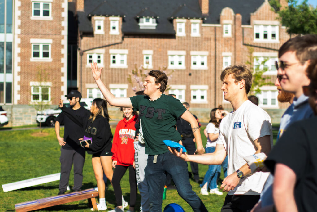 A college student in a fraternity shirt throws a beanbag