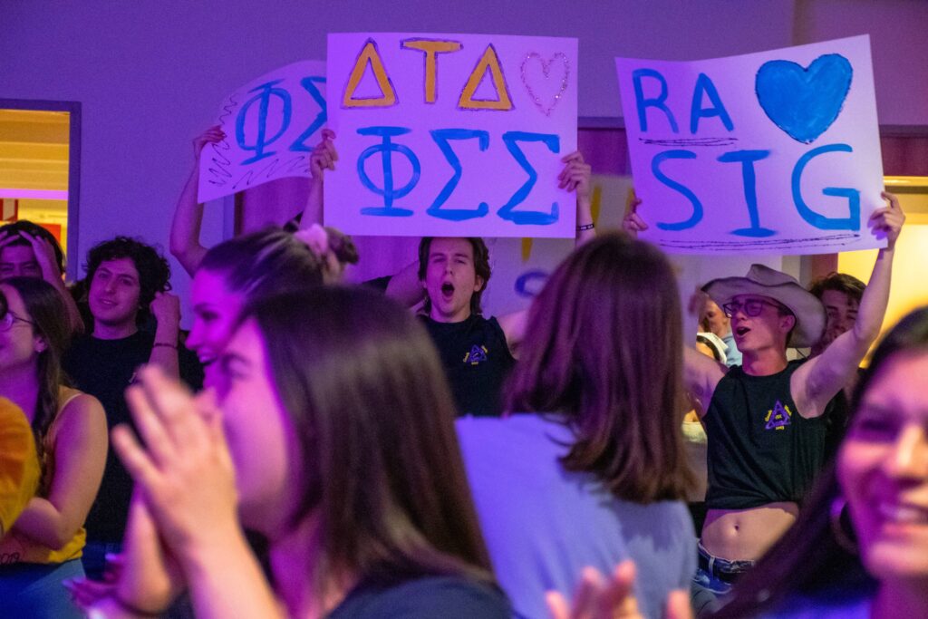 College students hold up signs with Greek letters on them