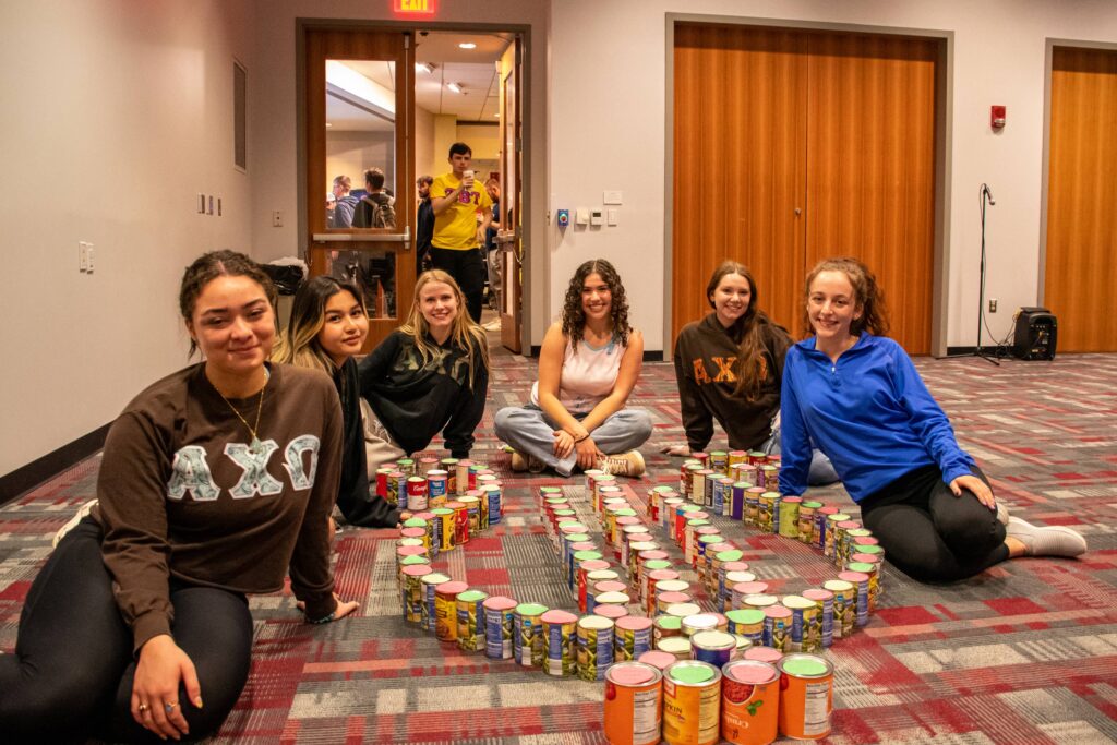 A group of sorority members smile next to cans arranged in a shape