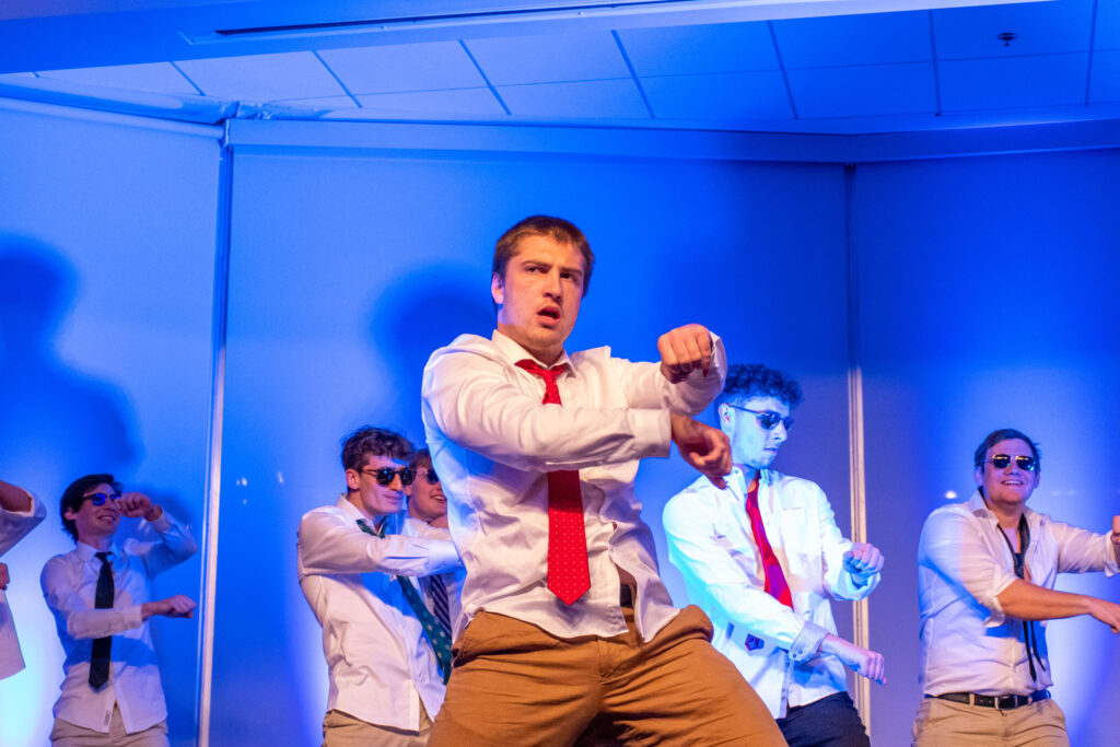 College students wearing white shirts and ties lip synch and dance