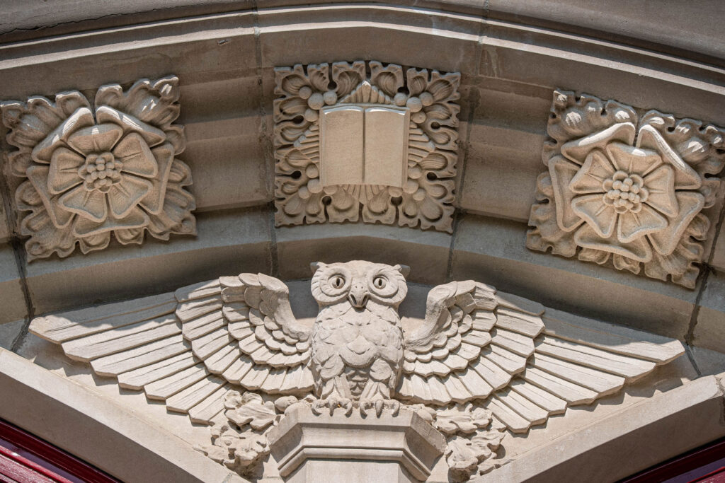 Close up photo of the stone details of an owl, luther rose, and book on a building