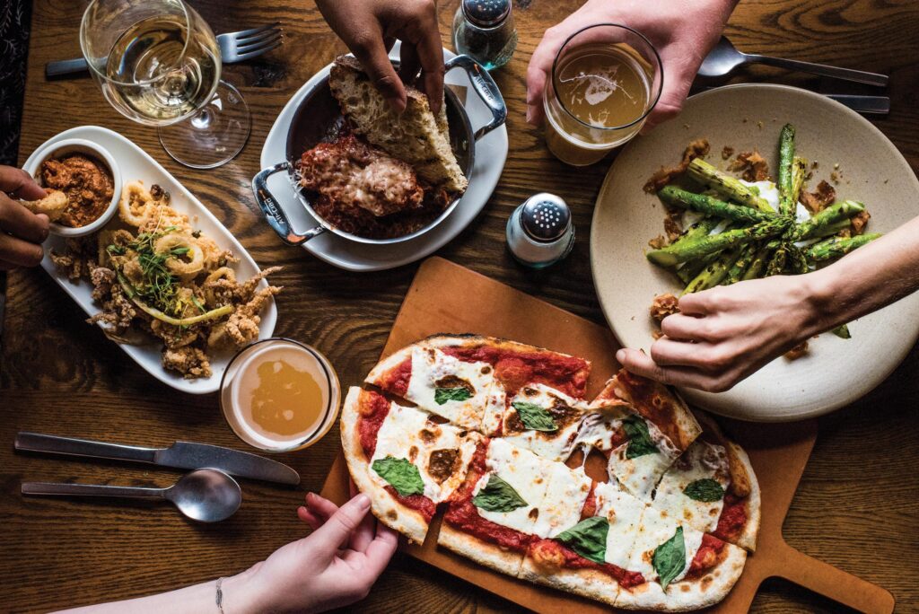 A photo taken from above with food on the table and hands reaching towards it