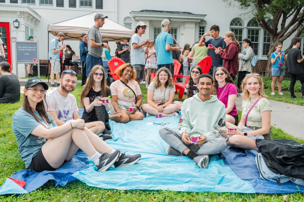 A circle of college students sit on the ground at a welcome event at the Leffell Center for Jewish Student Life