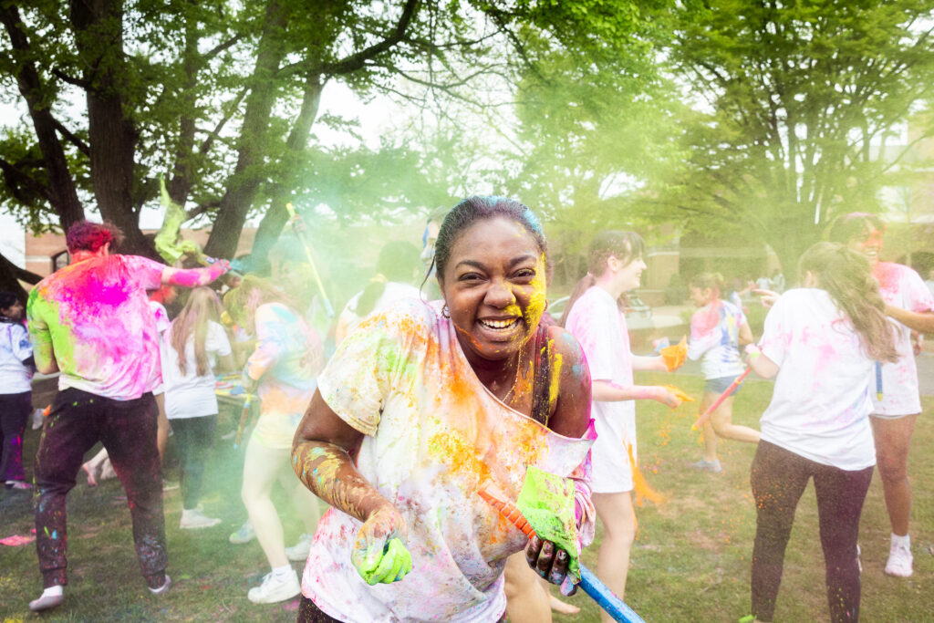 A college student smiles while covered in colorful powder