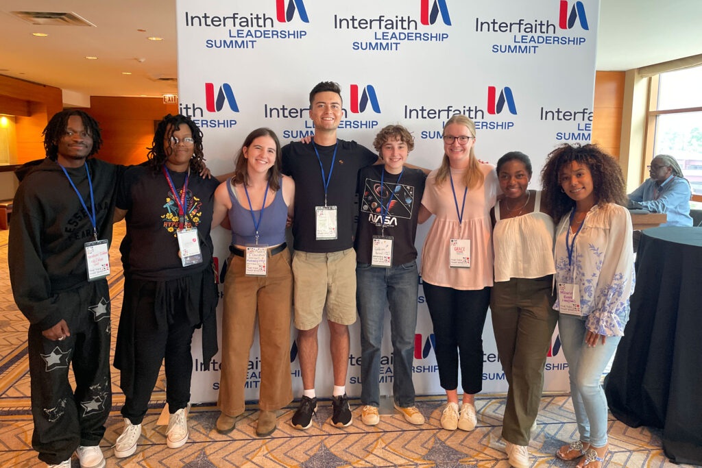 A group of college students stands in front of a sign that says Interfaith Leadership Summit